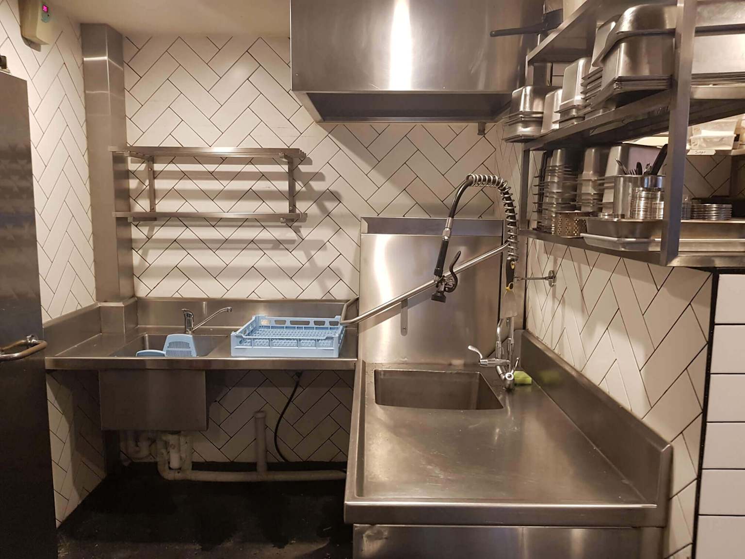 A well-organized commercial kitchen warewashing area featuring stainless steel sinks, a pre-rinse faucet, and shelving for kitchenware