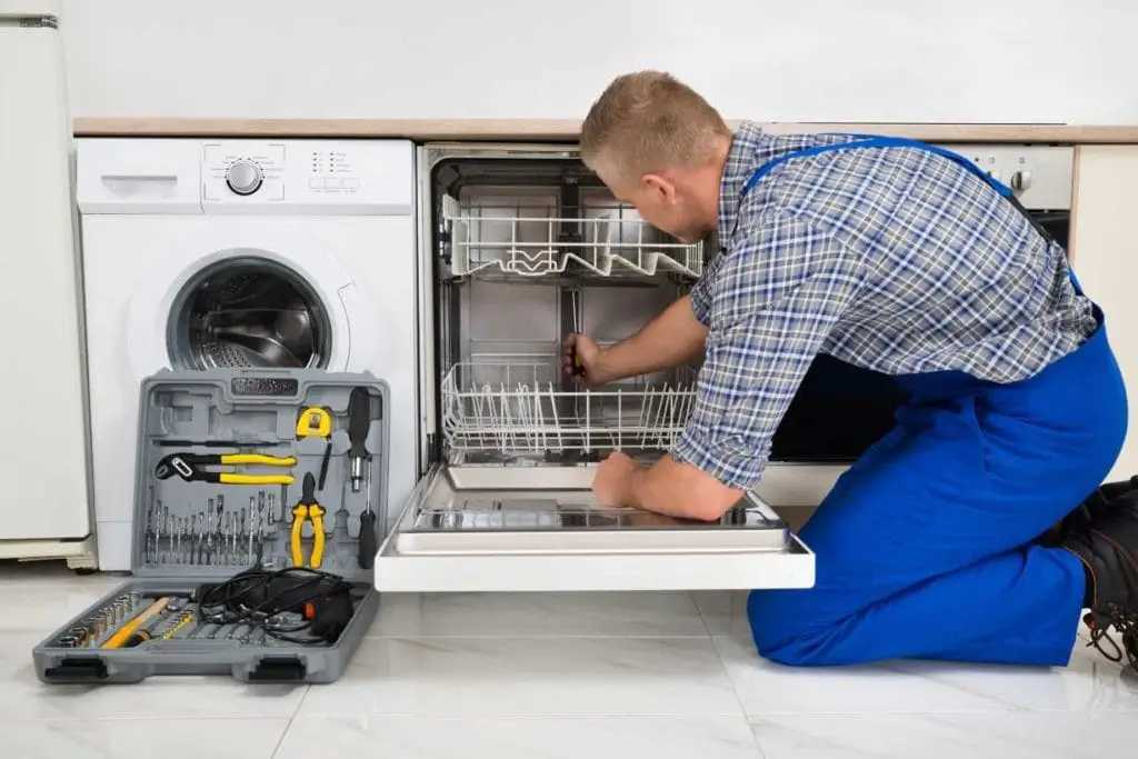 A technician performing repair work on a residential dishwasher in a kitchen setting