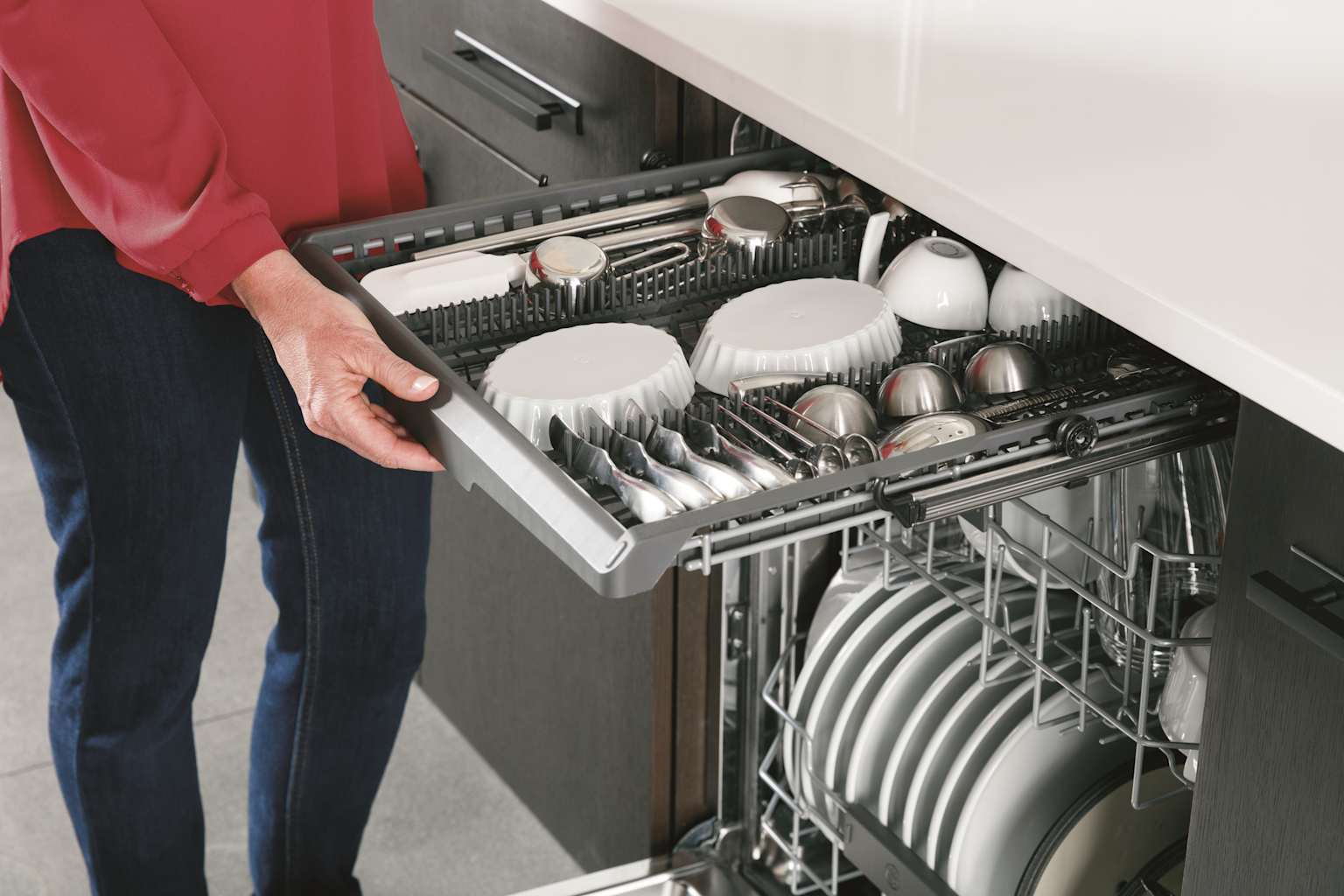 A person loads a dishwasher featuring a versatile third rack for cutlery and small kitchen items