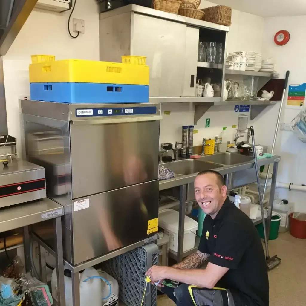 A technician from Cemco Service attends to a Cater-Wash commercial dishwasher in a professional kitchen